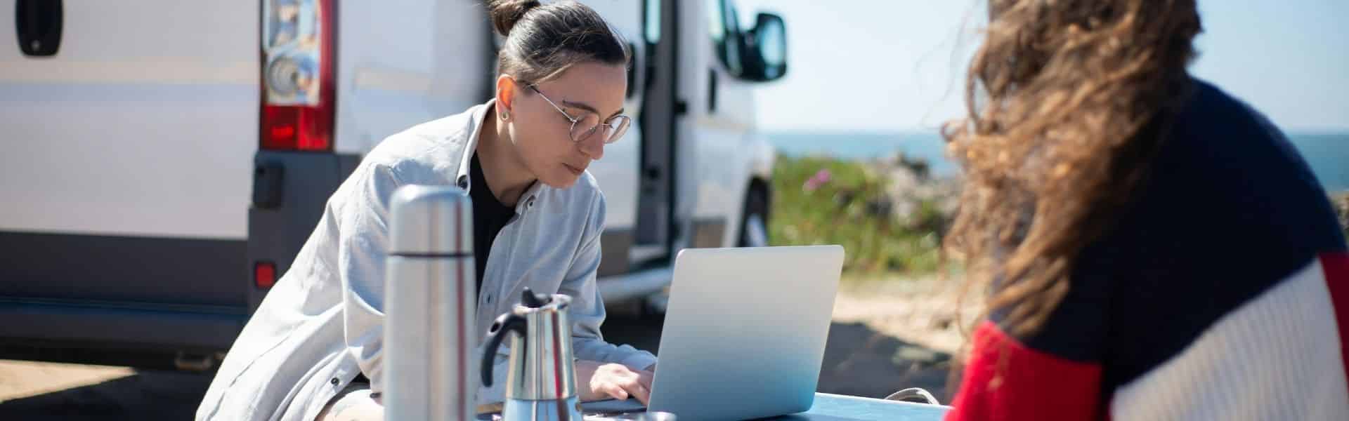 Person working on a laptop outdoors near a camper van, symbolising the freedom of digital nomads with visa programs